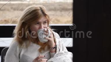 舒适的家居概念。 年轻女子坐在格子呢的开放式露台上享受热咖啡。 4千克